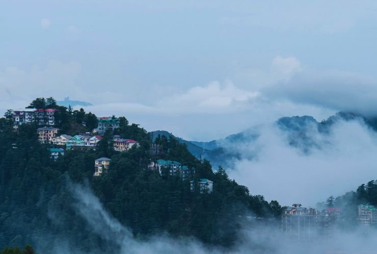 Foggy panoramic view of Shimla tourist places with red-roofed buildings on misty hills.
