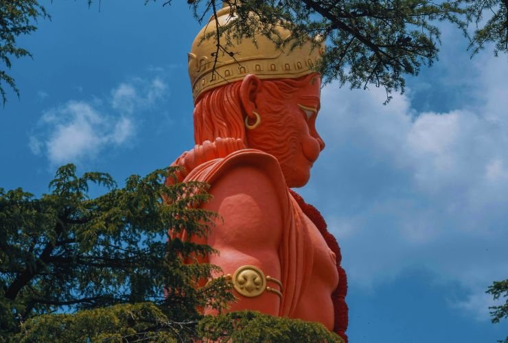 Majestic orange 108-foot Hanuman statue at Jakhoo Temple on Jakhu Hill, Shimla, surrounded by pine trees and blue sky, key Shimla tourist attraction.